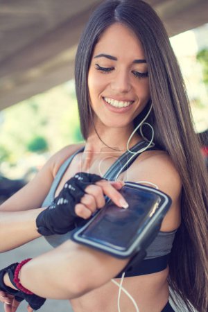 Photo for Runner touching the display touchscreen on armband with mobile phone to play music - Royalty Free Image