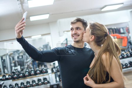 Téléchargez les photos : Beau couple sportif prenant une photo selfie avec téléphone intelligent à la salle de gym - en image libre de droit
