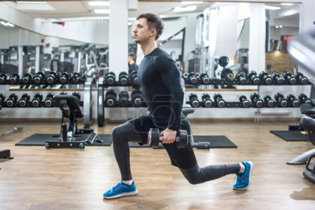 Téléchargez les photos : Jeune homme en forme beau faire des exercices avec des poids dans la salle de gym - en image libre de droit