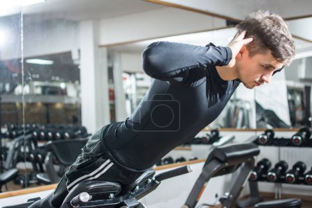 Téléchargez les photos : Jeune homme en forme beau effectuant un exercice d'hyperextension sur chaise romaine à la salle de gym - en image libre de droit