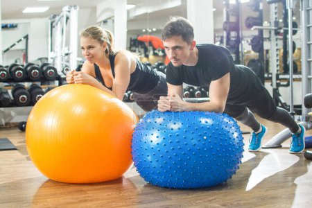Téléchargez les photos : Couple sportif faisant de l'exercice de planche sur des balles de fitness dans la salle de gym - en image libre de droit