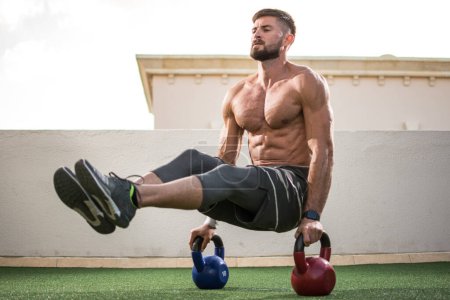 Photo for Muscular shirtless man workout with kettle bells in L Sit position at rooftop gym - Royalty Free Image