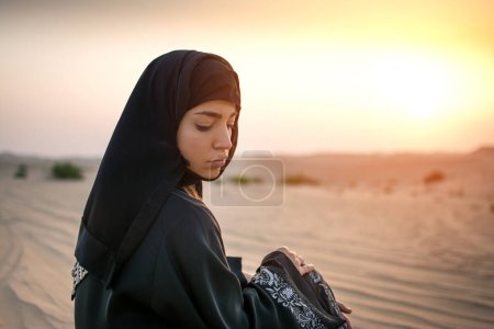 Téléchargez les photos : Portrait de la belle Arabe assise dans le désert au coucher du soleil - en image libre de droit