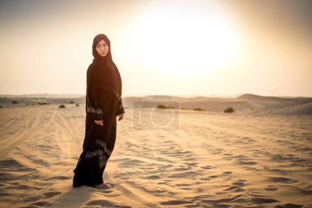 Téléchargez les photos : Femme arabe debout dans le désert pendant le coucher du soleil - en image libre de droit