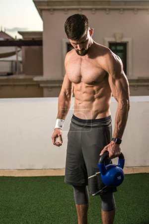 Photo for Muscular shirtless man holding kettle bell and preparing for weight training outdoors - Royalty Free Image