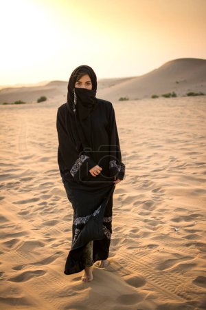 Téléchargez les photos : Arabe musulmane en tenue traditionnelle marchant dans le désert - en image libre de droit