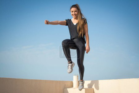 Foto de Mujer joven saltando sobre la pared contra el cielo azul - Imagen libre de derechos