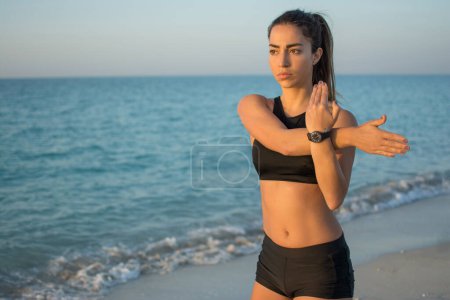 Foto de Retrato de chica deportiva delgada calentándose en la playa - Imagen libre de derechos