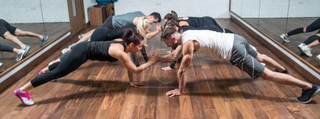 Photo for Panoramic view group of sporty people doing push ups and holding hands together while looking each other in gym - Royalty Free Image