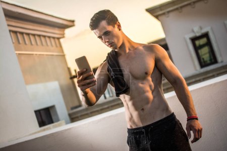 Téléchargez les photos : Bel homme torse nu avec chemise sur les épaules prenant un selfie avec téléphone portable après la formation en plein air - en image libre de droit