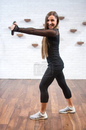 Téléchargez les photos : Souriant mince jeune femme faire des exercices avec du poids dans le club de fitness - en image libre de droit