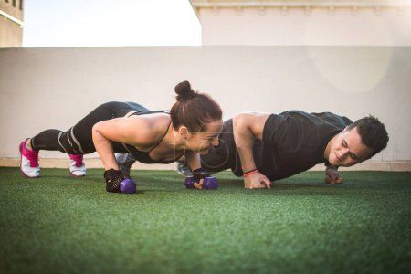 Photo for Beautiful fitness young sporty couple doing push ups together at outdoors gym - Royalty Free Image