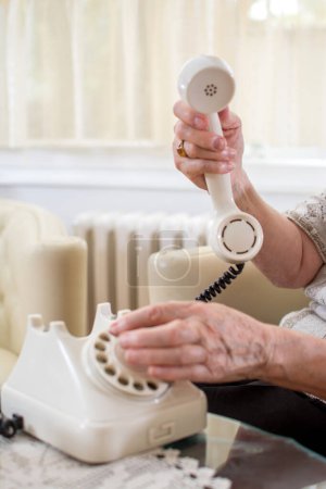 Foto de Primer plano de las manos arrugadas de las personas mayores marcando el número de teléfono en el teléfono giratorio en el ambiente pasado de moda - Imagen libre de derechos
