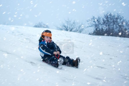 Photo for Cute little boy with saucer sleds outdoors on winter day. Excited child sledding down a hill - Royalty Free Image