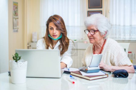 Téléchargez les photos : Infirmière regardant les résultats médicaux de sa patiente âgée sur ordinateur portable. Concept de soins à domicile - en image libre de droit
