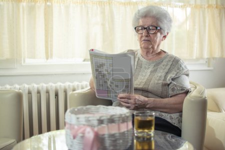 Foto de Mujer mayor resolviendo un crucigrama en casa - Imagen libre de derechos