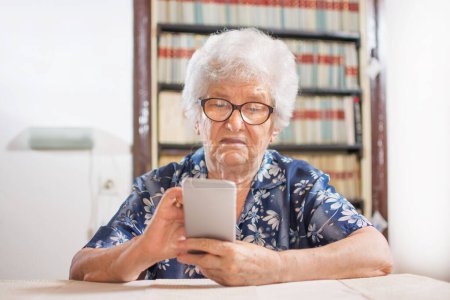 Foto de Mujer mayor mirando un teléfono inteligente en casa - Imagen libre de derechos
