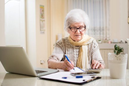 Téléchargez les photos : Femme d'affaires senior calculant les impôts à la maison - en image libre de droit