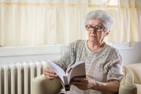 Foto de Anciana leyendo un libro en casa - Imagen libre de derechos