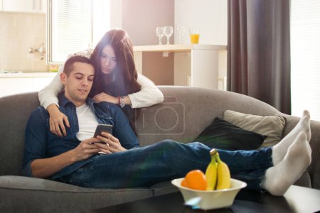 Junges Paar schaut im Wohnzimmer aufs Smartphone