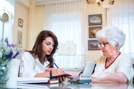 Téléchargez les photos : Aide-soignant examinant la pression artérielle du patient âgé à la maison - en image libre de droit