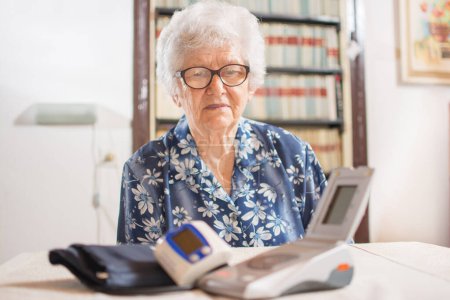 Foto de Mujer mayor mirando el monitor digital de presión arterial en la mesa - Imagen libre de derechos