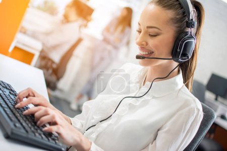 Foto de Retrato de una hermosa mujer de negocios sonriente con auriculares usando computadora en la oficina - Imagen libre de derechos