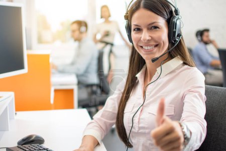 Photo for Portrait of beautiful young woman wearing headset showing thumbs up gesture. Customer support service agent woman working in call center and showing success sign with a hand. - Royalty Free Image