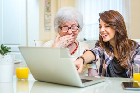 Foto de Nieta señalando algo en la pantalla del ordenador portátil a su abuela en casa - Imagen libre de derechos