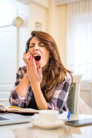 Téléchargez les photos : Fatiguée somnolente étudiante bâillant, travaillant au bureau et tenant un stylo - en image libre de droit