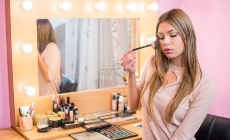 Téléchargez les photos : Adolescente appliquant de la poudre à l'aide d'une brosse de maquillage à la maison - en image libre de droit