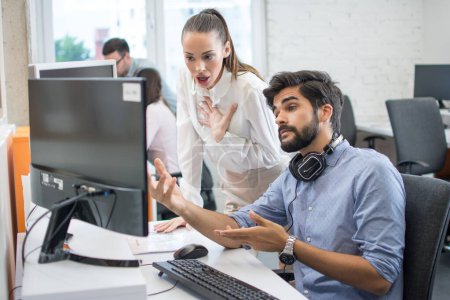 Überraschte junge Geschäftsfrau und gutaussehender junger Geschäftsmann schaut im Büro auf Computerbildschirm