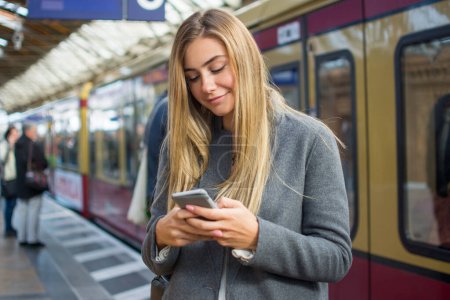 Téléchargez les photos : Portrait de jeune femme utilisant le téléphone à la gare - en image libre de droit