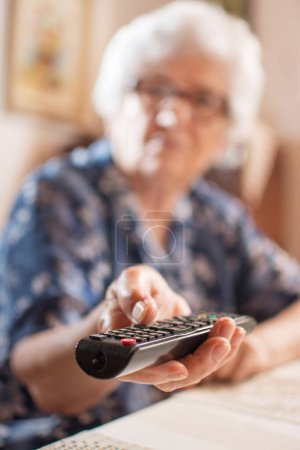 Téléchargez les photos : Gros plan des mains de femme âgée tenant télécommande de télévision. Concentration sélective - en image libre de droit