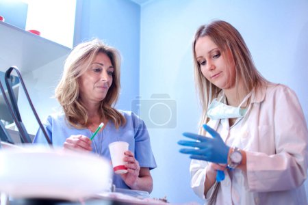Téléchargez les photos : Jeune dentiste portant des gants chirurgicaux et se préparant à l'examen dentaire avec l'aide d'un collègue plus âgé dans une clinique dentaire. - en image libre de droit