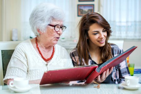 Grandma and her granddaughter looking at photo album together at home