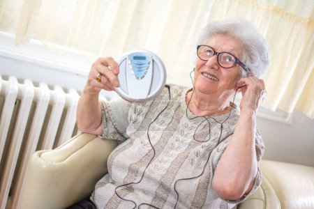 Foto de Feliz mujer mayor escuchando música en el reproductor de mp3 en casa - Imagen libre de derechos