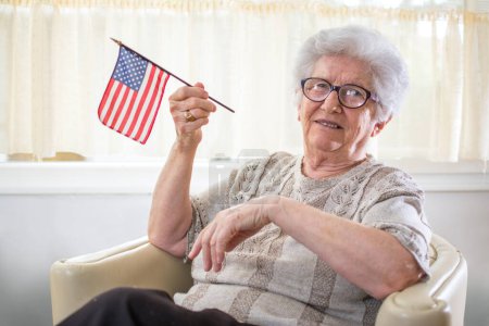 Téléchargez les photos : Femme âgée souriante tenant le drapeau américain et célébrant la fête de l'indépendance américaine - en image libre de droit