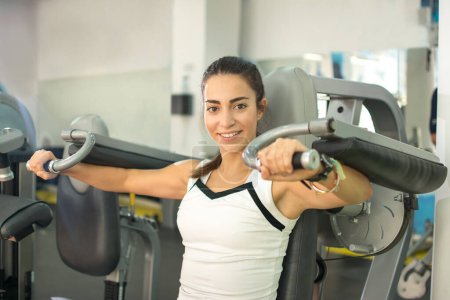 Téléchargez les photos : Jeune femme faisant des exercices sur la machine de gymnase de presse de poitrine dans le centre de fitness - en image libre de droit