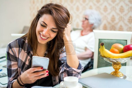 Foto de Mujer joven usando el teléfono y sonriendo mientras pasa tiempo en casa de las abuelas - Imagen libre de derechos