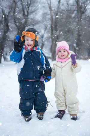 Téléchargez les photos : Petit garçon et fille saluant tout en profitant d'une journée d'hiver enneigée - en image libre de droit
