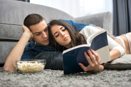 Téléchargez les photos : Jeune couple lisant un livre par terre à la maison - en image libre de droit
