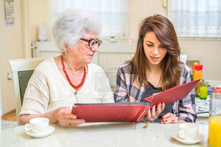 Photo for Grandma and her granddaughter looking at photo album together at home - Royalty Free Image