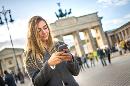 Foto de Mensajería de texto hermosa chica de pie cerca de la Puerta de Brandeburgo en Berlín, Alemania - Imagen libre de derechos