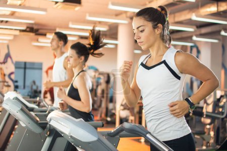 Téléchargez les photos : Jeune femme courir sur un tapis roulant à la salle de gym - en image libre de droit