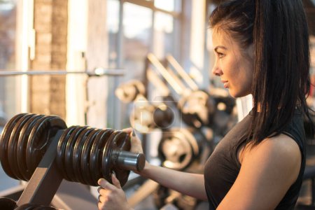 Téléchargez les photos : Jeune femme qui choisit des poids pour son entraînement en salle de gym - en image libre de droit