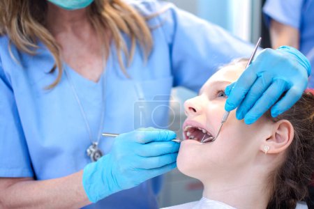 Téléchargez les photos : Fille à bouche ouverte ayant ses dents examinées par un spécialiste. Vérification des dents au cabinet des dentistes - en image libre de droit