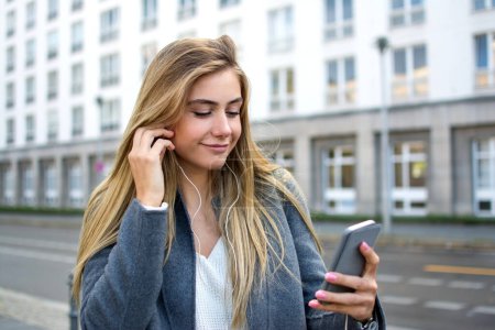 Foto de Hermosa chica con teléfono inteligente y auriculares escuchando música en la calle de la ciudad - Imagen libre de derechos