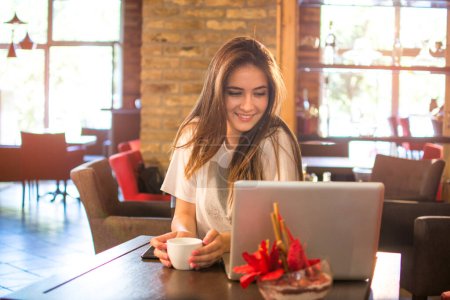 Téléchargez les photos : Adolescente boire du café et regarder ordinateur portable dans un café - en image libre de droit