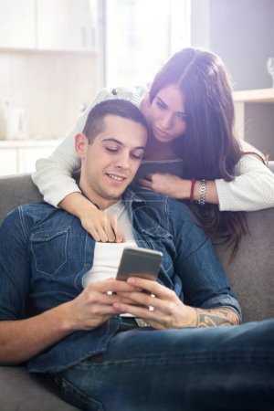 Junges Paar schaut zu Hause gemeinsam aufs Smartphone